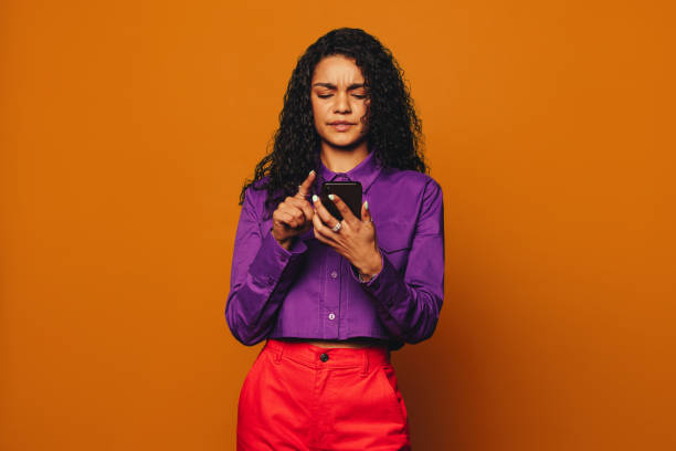 istock Vibrant woman confused while messaging on orange background with modern smartphone 2097370586