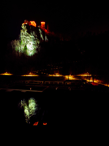 Lake Bled at night with clear reflection of illuminated Bled castle on calm water surface. Waterfront with street lights. Date: 19.12.2023, Bled, Slovenia.