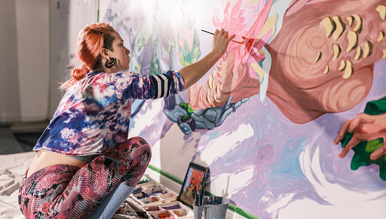 Young Caucasian woman creating indoor mural at the gym. She is dressed in casual outfit. Interior of small gym in the city of Toronto, Canada..