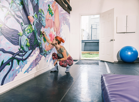 Young Caucasian woman creating indoor mural at the gym. She is dressed in casual outfit. Interior of small gym in the city of Toronto, Canada..