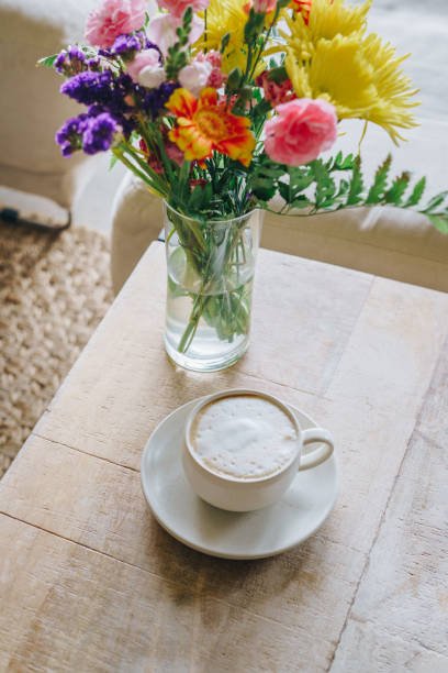 A ceramic cup with cappuccino on a rustic wooden table. Colorful bouquet of flowers on the table.