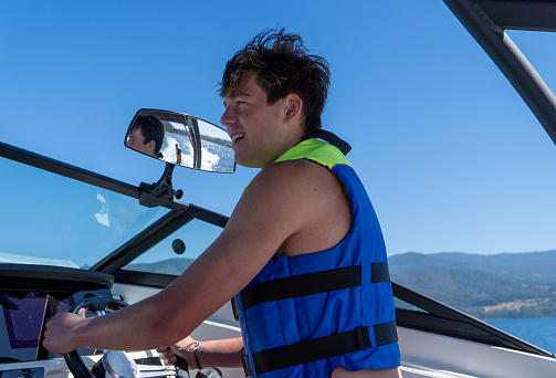 Portrait of a young brunette man driving a boat with a smile, learning to navigate.