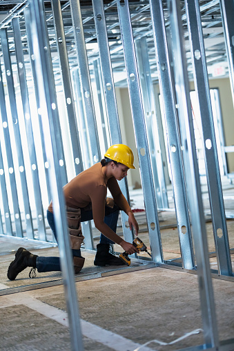 A young African-American woman wearing a hardhat working at a construction site, an office space being renovated for a new tenant.