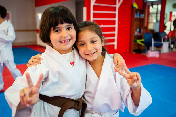 two elementary age children are taking a martial arts class. They are standing together in a row and are smiling while looking at the camera. A group of elementary age children are taking a martial arts class. They are standing together in a row and are smiling while looking at the camera, Peace Sign - Gesture, martial arts stock pictures, royalty-free photos & images