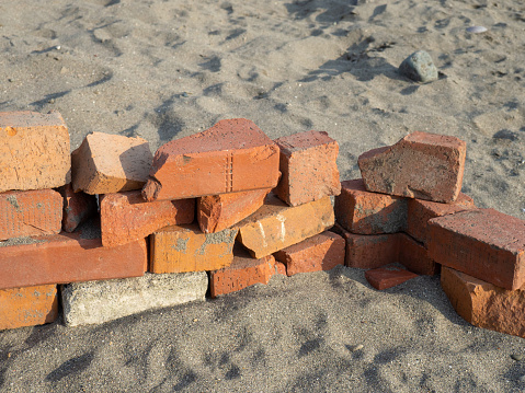 Old red bricks stacked on the sand. Broken bricks. Building materials unsuitable for use