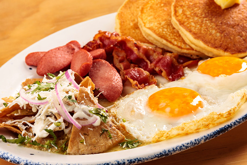 Full American breakfast with eggs, bacon, pancakes, sausage and chilaquiles, food