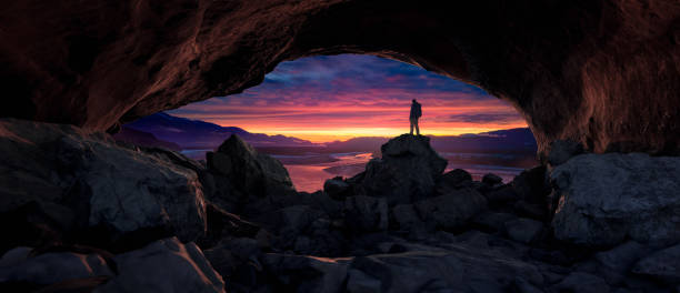 istock Adventure Man Standing in Rocky Cave. Mountains and River in Background. 2097644863