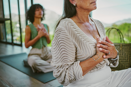 Close-up of a mature woman holding her chest chakra while meditating with her eyes closed during a yoga class at a wellness retreat