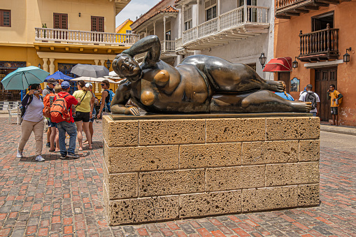Cartagena, Colombia - July 25, 2023: Colonial facades with wooden balconies around San Domingo Square with La Figura Reclinada bronze statue. People in photo