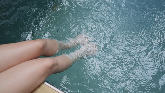 Closeup of beautiful female legs in water of a pool woman relax casual sit on wooden terrace deck