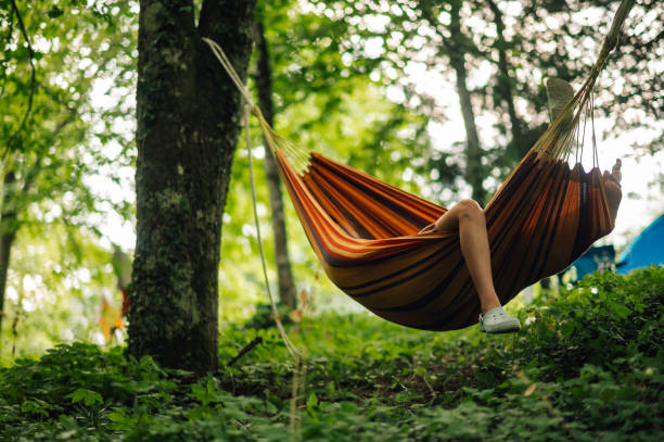 A leg hanging from a hammock in camp site in forrest. People resting in hammock in camp site in a forrest.. A leg is hanging from hammock. People sleeping and resting from concerts and wild night on a music open air summer festival. hammock stock pictures, royalty-free photos & images