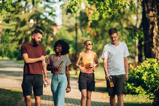 Three quarter length of multicultural friends walking in city park and having fun time together. An interracial urban crew is spending quality time together in city park and walking towards camera.