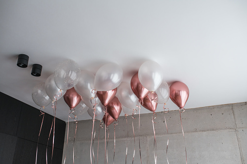 Pink and white balloons cover the ceiling of a hotel bedroom, creating a festive atmosphere before the celebration.
