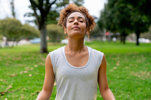 Peaceful African American woman meditating outdoors at the park