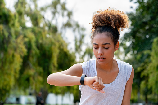 Young African American woman running outdoors and checking her fitness tracker