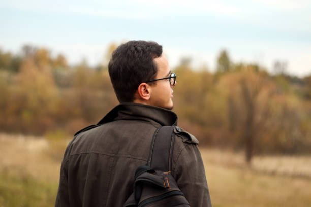 Back view tourist adventurous man with backpack stands on fall nature background. Man enjoys inspiring epic landscape. Blurred.