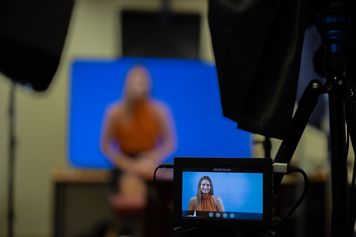 Professional young female in a recording studio. Media training for interview, video recording, live broadcast, social media, news journalism, education. Close up shot of recording camera equipment with person in background blurred out.
