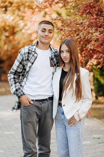 Vertical photo of two teenage friends dressed in casual clothes standing next to each other against a background of nature. Best school friends are ready to overcome anything to achieve the goal.