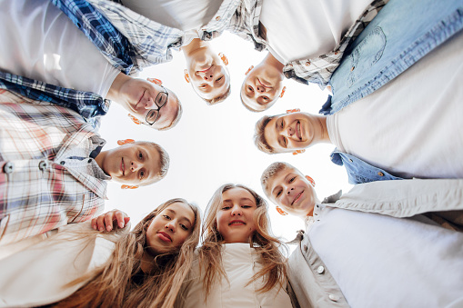 Large group of smiling young people standing, hugging, looking at camera. Group of cheerful teenage people in a circle looking down. Low viewing angle. Copy space.