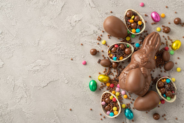 istock Delightful Easter assortment showcased from top view: Broken chocolate shells revealing vibrant candies, alongside a chocolate rabbit on a grey concrete backdrop, space for text 2097857761