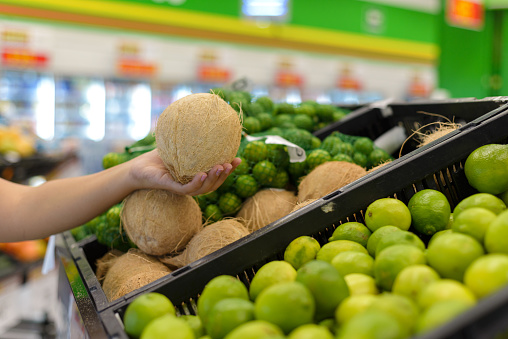 Hand holding a coconut in a supermarket.