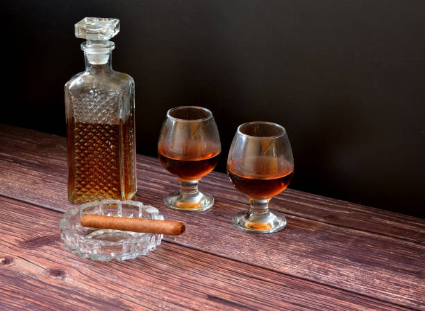 a crystal decanter and two glasses of cognac on a dark wooden table, next to a cuban cigar in a glass ashtray. - decanter crystal carafe glass imagens e fotografias de stock