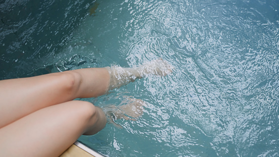Closeup of beautiful female legs in water of a pool woman relax casual sit on wooden terrace deck