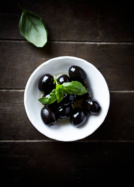 Black olives with fresh basil on rustic wooden background. Soft focus. Close up.