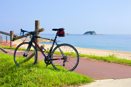 Goseong County, South Korea - July 30, 2019: A solitary bike leans against a wooden fence on Bongpo Beach, facing the pristine, rocky greenery of the uninhabited Jukdo Island on a warm summer day.