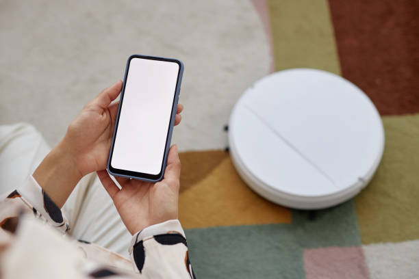 istock Woman Holding Smartphone Operating Robot Vacuum 2098119687