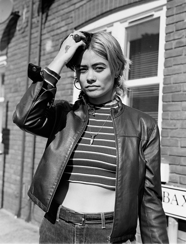 Analog portrait of mixed race woman in the street of London. It is a monochrome image made with a medium format film camera in a sunny day. She is wearing a leather jacket.