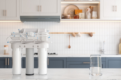 Close-up View Of Reverse Osmosis Water Filtration System And Glass Of Water On Kitchen Counter With Blurred Background