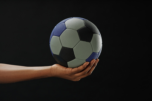 Minimal close up shot of hand holding football ball against black background with copy space