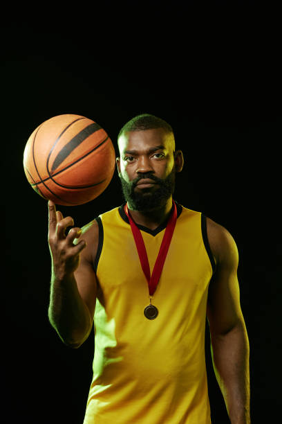 Vertical waist up portrait of African American basketball player wearing gold medal and spinning ball