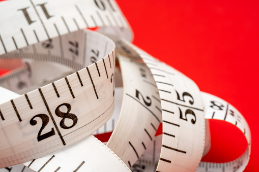 White measuring tape on red background. Measurement of length and circumference. Lose weight and get fat.