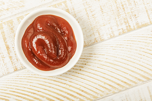 Flat Lay close up of a dish of delicious Ketchup isolated on a wooden background with copy space