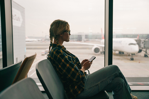 Female passenger waiting for flight at airport lounge and using smart phone