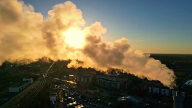Steaming chimney vapour emissions floating across factory refinery during sunset aerial drone footage