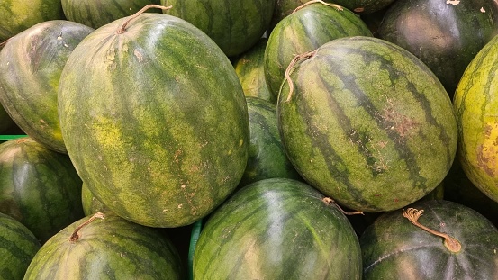 Pile of fresh watermelons (Citrullus lanatus) on the market. Watermelon is a sweet, commonly consumed fruit of summer. Watermelon juice can be blended with other fruit juices or made into wine.