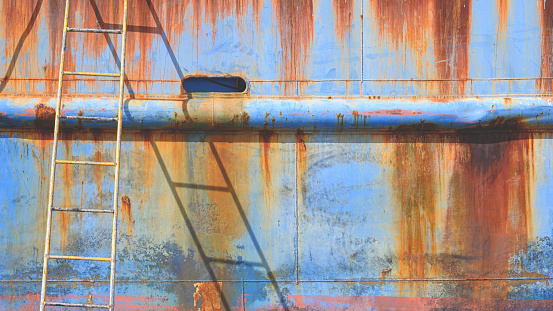 Rusty metal hull of the old nautical vessel with ladder at shipyard during improvement and renovation work