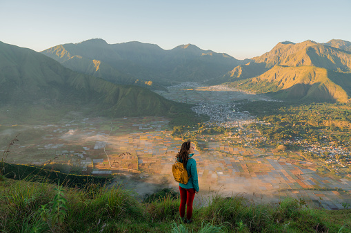 Woman  with backpack standing on viewpoint after hike near mount Rinjani on Lombok island