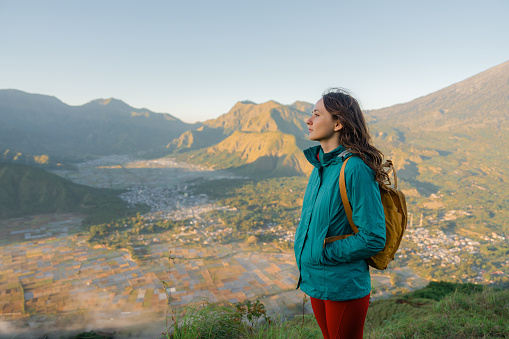 Woman  with backpack standing on viewpoint after hike near mount Rinjani on Lombok island