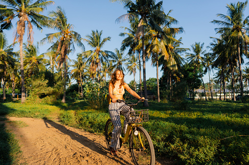 Cheerful woman riding bicycle through coconut grove  on Gili Trawangan during beach vacation in Indonesia