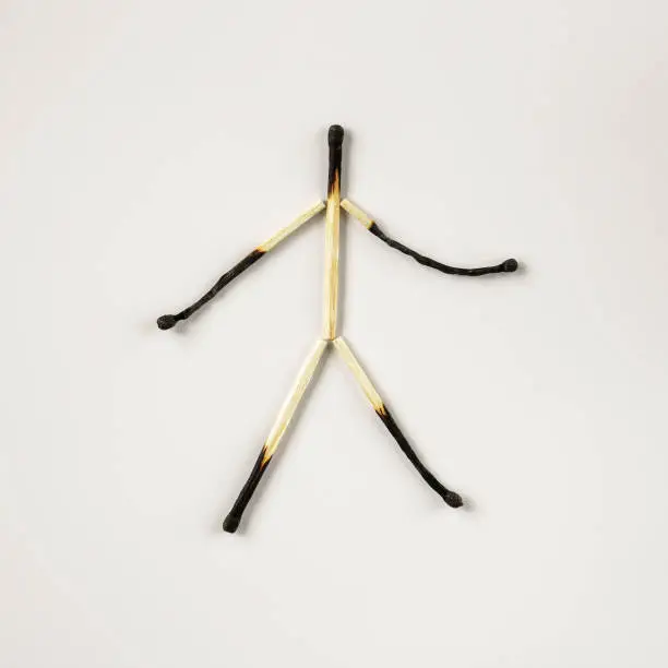 Photo of A human figure made of burnt charred matches on a white background. The concept of emotional burnout.