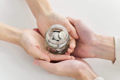 Hands of a man and woman carrying a jar containing coins