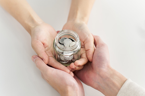 Hands of a man and woman carrying a jar containing coins