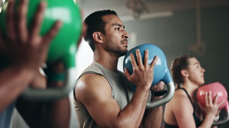 Gym, group fitness and kettlebell squat exercise for power, sports challenge and muscle. Serious asian man, bodybuilder and heavy weights for training in health club, workout class and strong friends