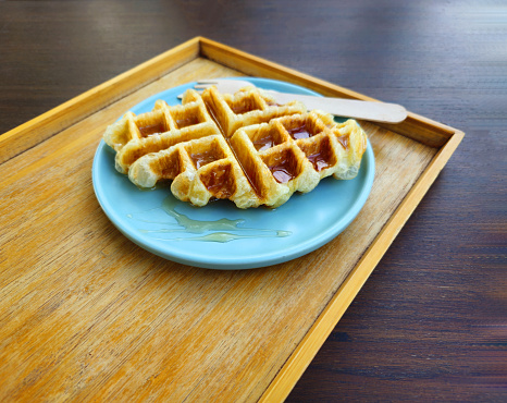 Waffle topped with honey sauce on blue plate at cafe. Sweet bakery on dish with copy space.