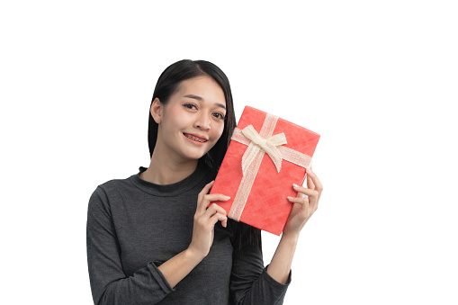 A woman is holding a red present with a bow on it. She is smiling and she is happy. Isolated on white background.
