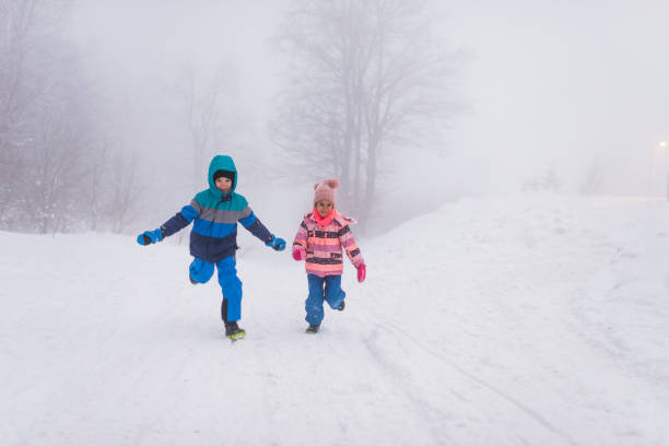 Winter portrait of a beautiful little boy and girl laughing and having a lot of fun in snow.